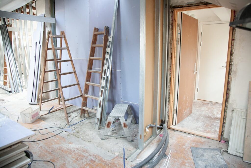 Home renovation with ladders, drywall, and tools in a partially constructed room.