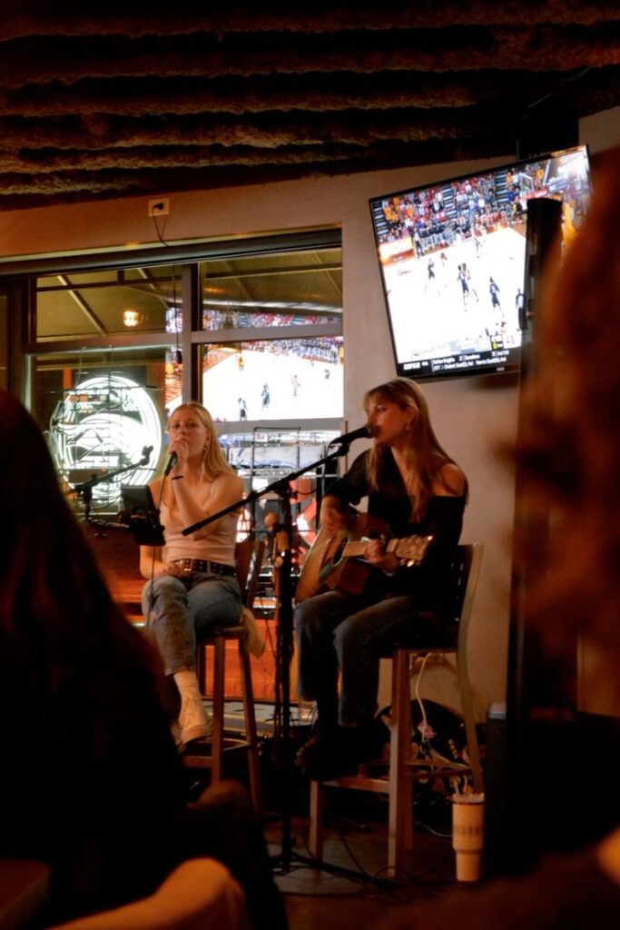 Live acoustic performance by two musicians in a cozy bar setting with sports on TV.