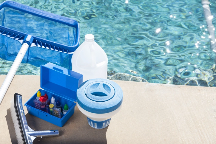 Pool maintenance supplies next to a sparkling blue swimming pool on a sunny day.