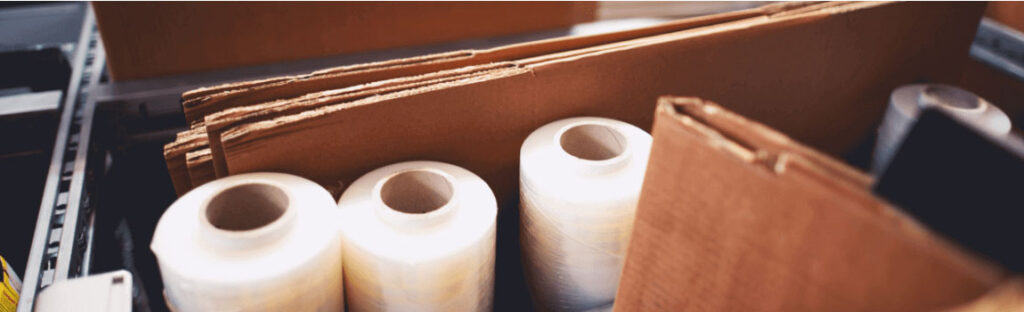 Cardboard boxes and rolls of packaging film in a warehouse setting for shipping and storage solutions.