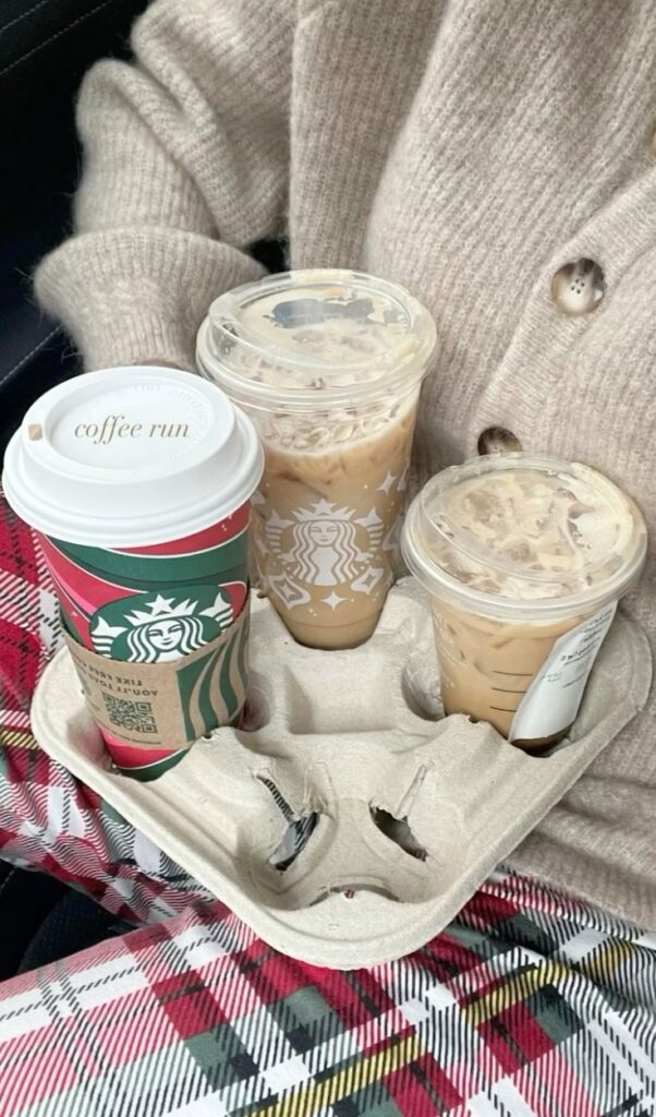 Cozy coffee run with Starbucks drinks in a tray, held by a person wearing a plaid outfit and fuzzy sweater.