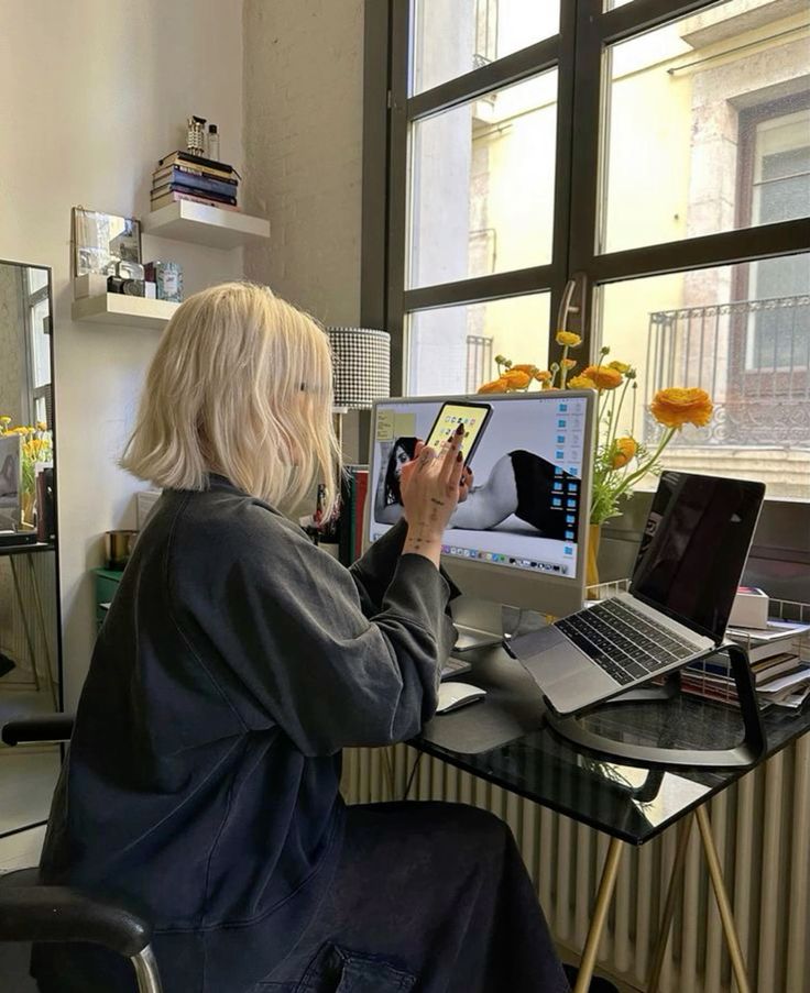 Woman taking mirror selfie with smartphone, holding a laptop and wallet, in modern bathroom setting.