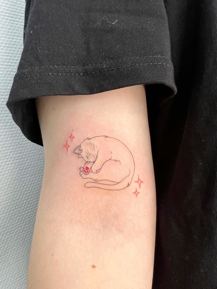 Minimalist cat tattoo on arm with pink stars, featuring a sleeping cat curled up with a pink paw print.