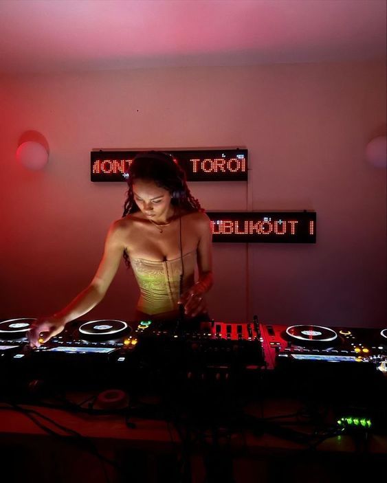 DJ performing live set in ambient red-lit room with sound equipment.