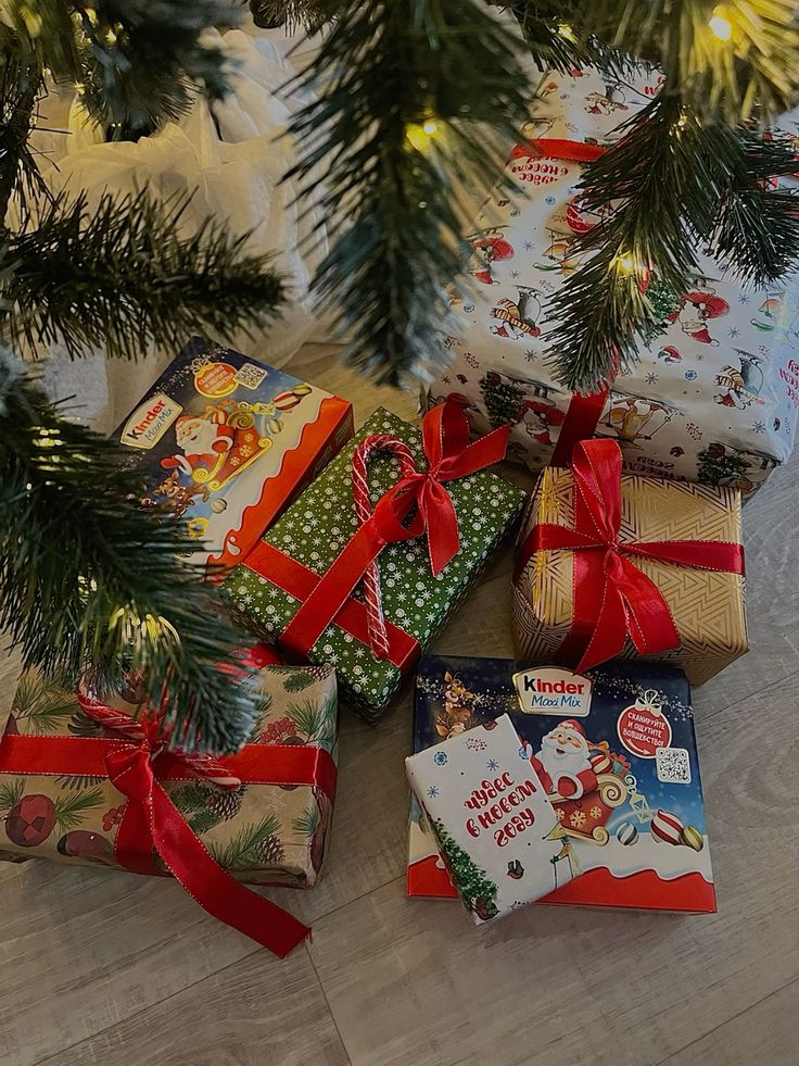 Новый год Christmas gifts with red ribbons under a decorated tree, featuring festive wrapping and Kinder chocolate. | Sky Rye Design Christmas gifts with red ribbons under a decorated tree, featuring festive wrapping and Kinder chocolate.
