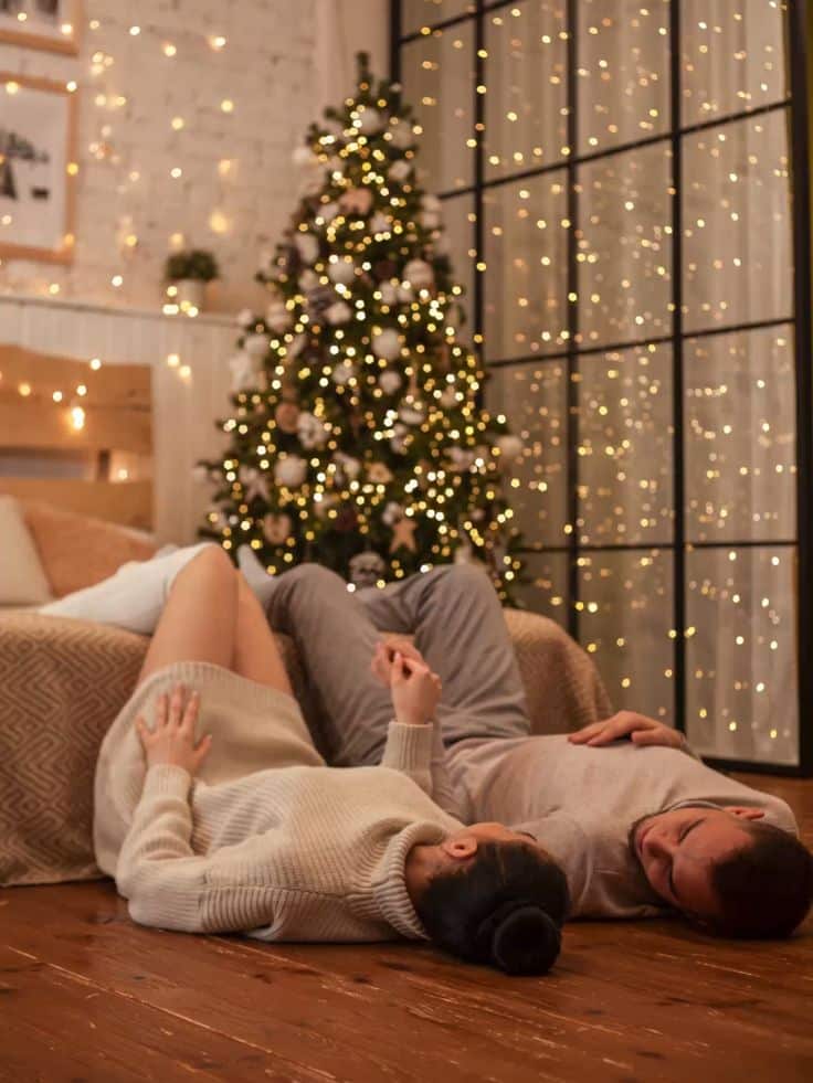 Парная новогодняя фотосессия Couple relaxing by a Christmas tree with festive lights and cozy decor in a warm living room. | Sky Rye Design Couple relaxing by a Christmas tree with festive lights and cozy decor in a warm living room.