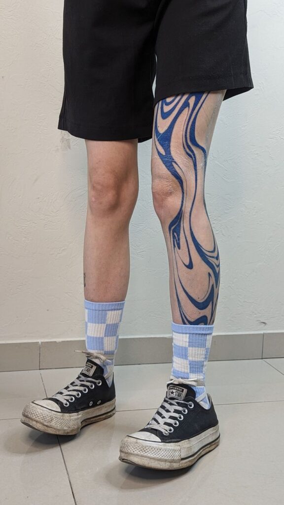 Person with artistic blue swirl leg tattoo, wearing checkered socks and black sneakers.