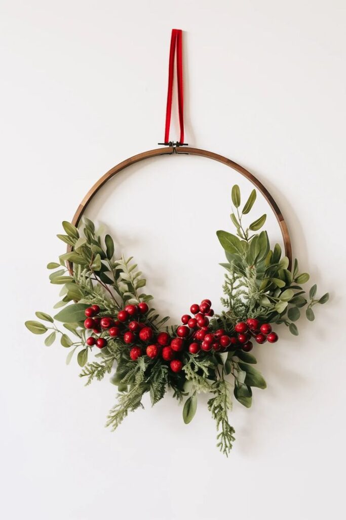 Minimalist holiday wreath with red berries and green foliage on a wooden hoop, hung by a red ribbon.