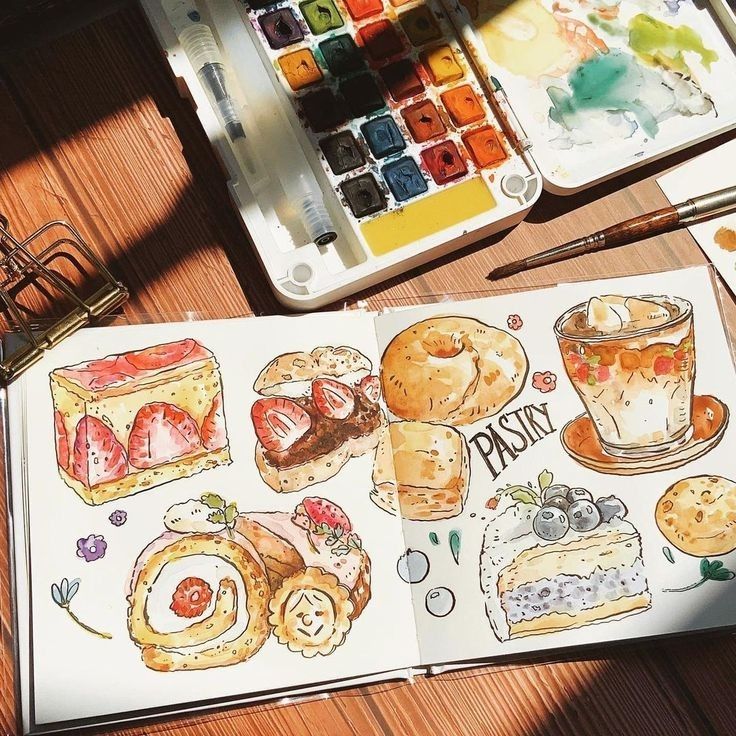 Watercolor pastry sketches with paint palette on wooden table.