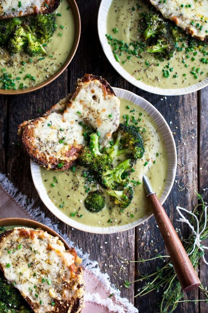 Bowl of creamy broccoli soup with cheesy bread, garnished with fresh herbs on a rustic wooden table.