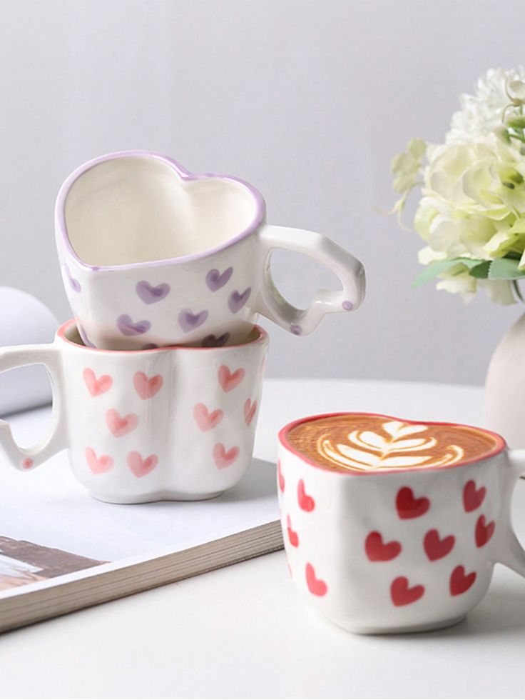 Heart-patterned mugs with latte art on table next to flowers, creating a cozy and romantic vibe.