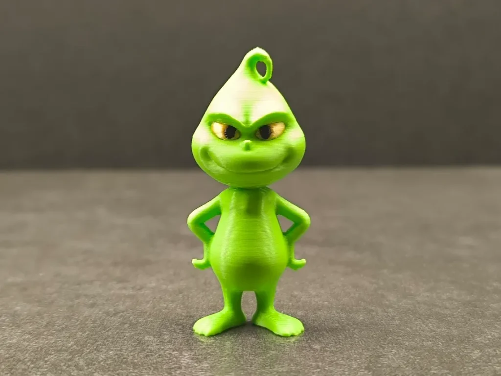 Green cartoon character figurine with mischievous smile, standing on a gray surface against a dark background.