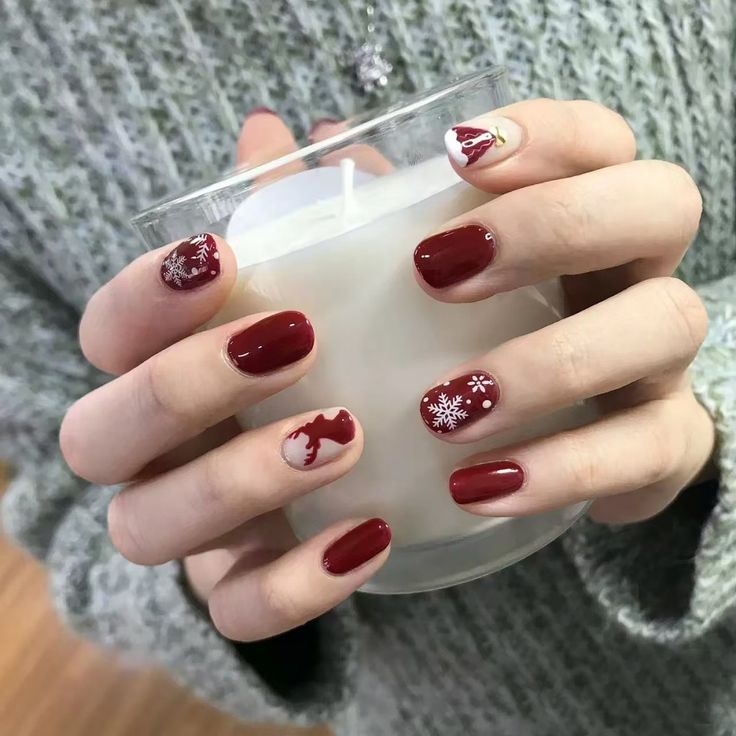 Festive red nail art with snowflake designs holding a white candle.