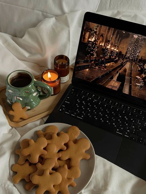 Cozy setup with gingerbread cookies, hot drink, candle, and holiday movie on a laptop in bed. Perfect winter retreat.