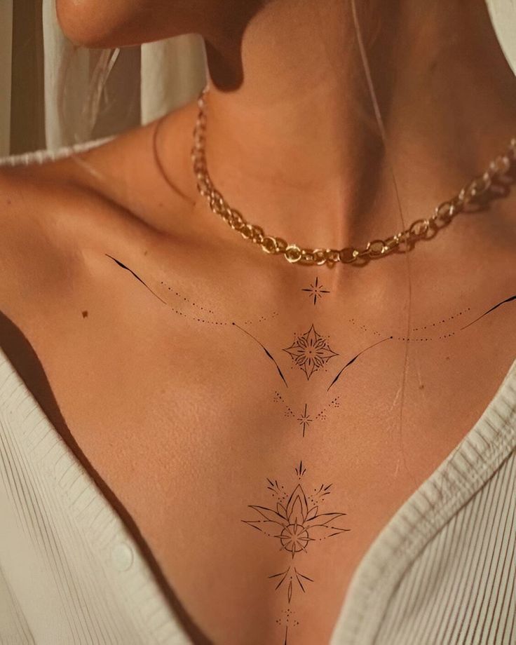 Close-up of a delicate floral chest tattoo design with a gold chain necklace and white blouse.