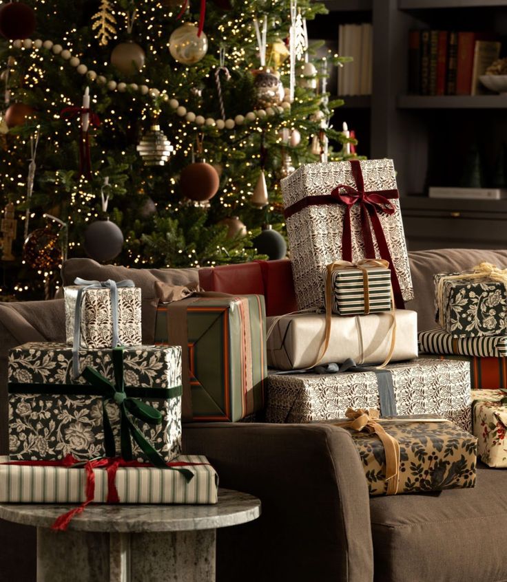 Stacks of beautifully wrapped Christmas gifts under a decorated tree in a cozy living room setting.