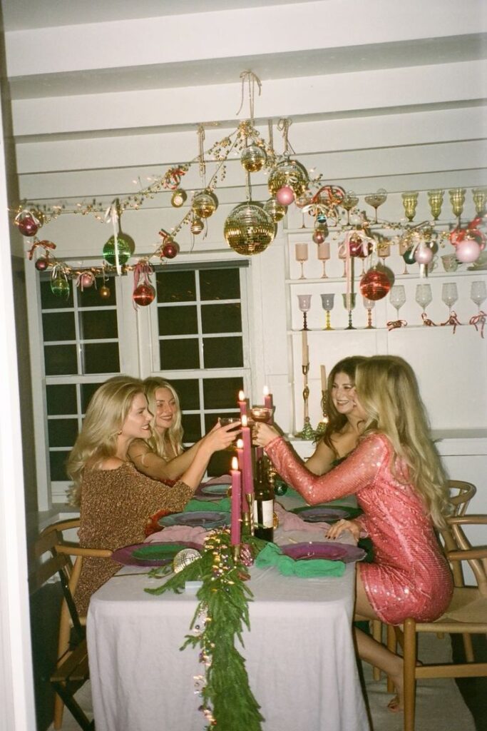 Festive gathering with women toasting at a decorated table adorned with colorful ornaments and hanging glassware.