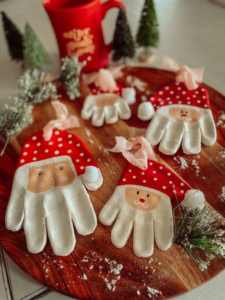 Handmade Santa ornaments shaped like gloves on a wooden tray, surrounded by small trees and a red holiday mug.