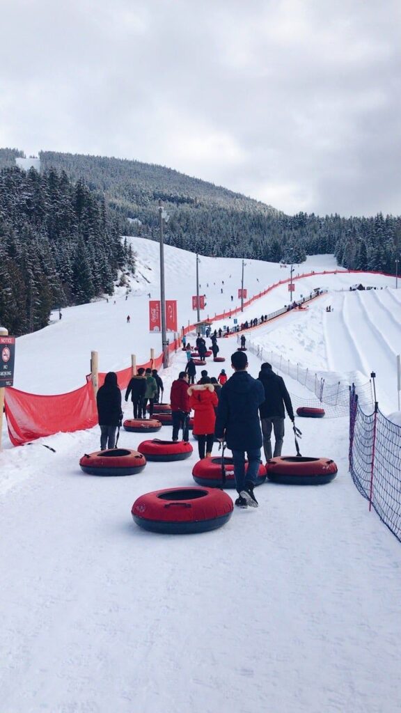 Winter fun at a snow tubing park with people pulling red tubes up a snowy hill.