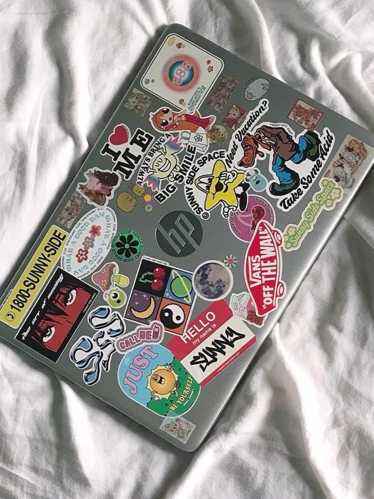 Laptop covered in vibrant, quirky stickers showcasing personality on a white bedspread.