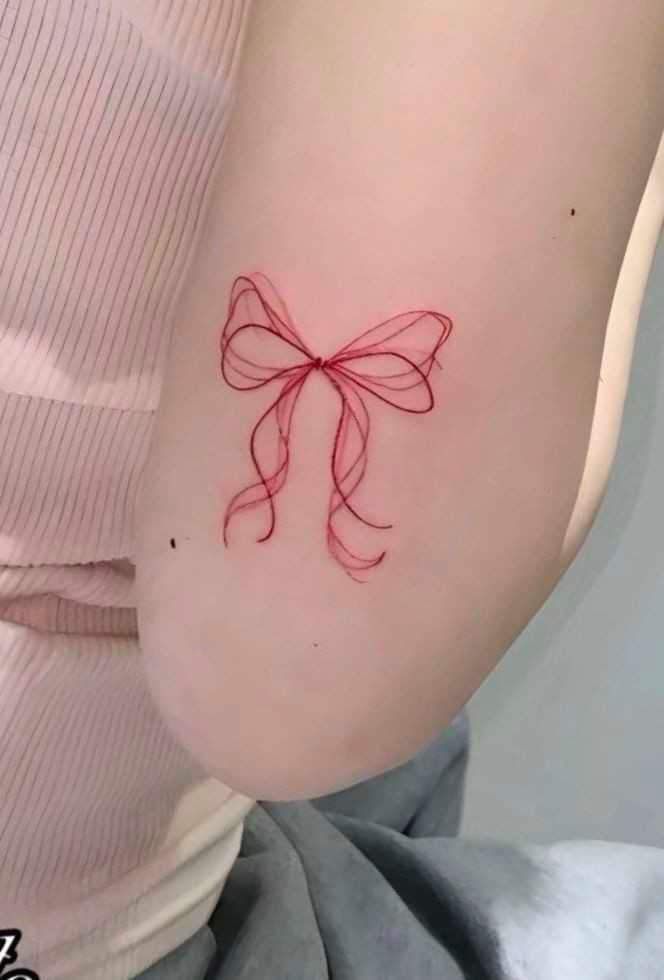 Delicate red bow tattoo on arm, showcasing intricate line art and elegant design.