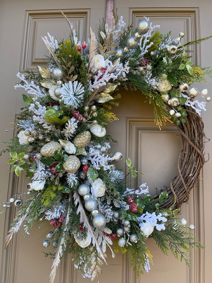 Festive holiday wreath with white flowers, red berries, and gold accents on a wooden door.