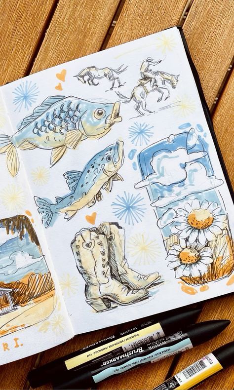 Sketchbook art with fish, cowboys, clouds, daisies, and cowboy boots, on a wooden table with markers.