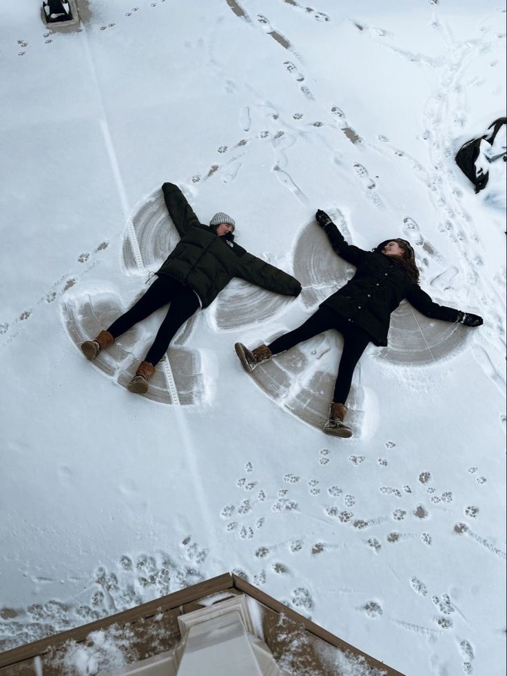 Two people making snow angels in fresh snow, surrounded by footprints, wearing winter coats and boots.