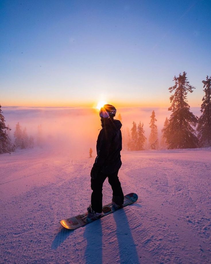 Snowboarder at sunrise on snowy slope, surrounded by trees and vibrant sky, capturing a breathtaking winter panorama.