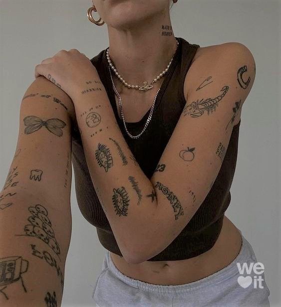 Person with multiple small tattoos on arms and neck, wearing a black tank top and necklace.