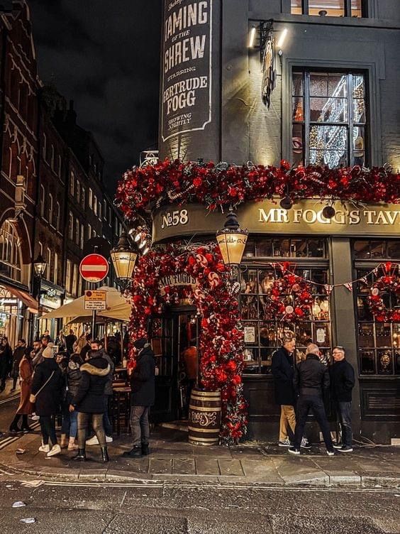 Festively decorated pub exterior at night with people gathering outside.