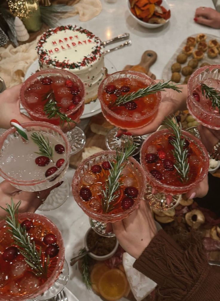 Festive holiday drinks with cranberries and rosemary, surrounded by a holiday cake and snacks.