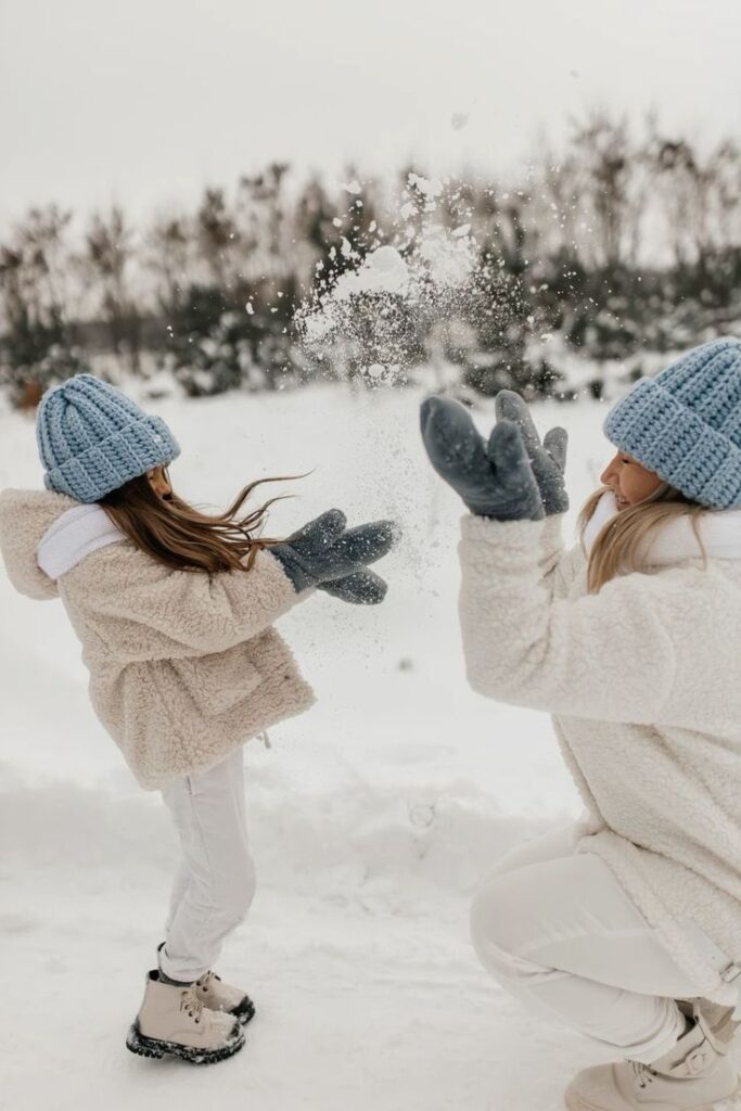 Mother and daughter in winter clothes having a snowball fight outdoors in a snowy landscape.