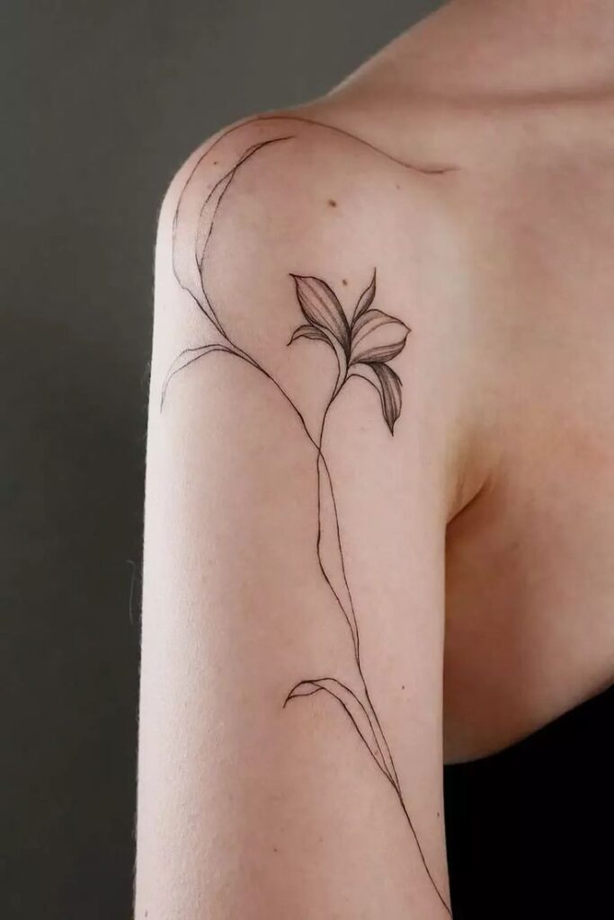 Minimalistic floral tattoo on upper arm, featuring a delicate line-art flower design on skin.