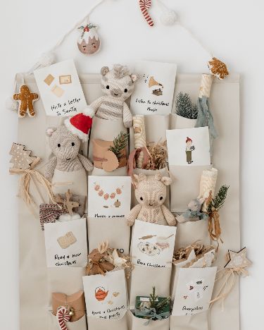 Advent calendar with plush toys and festive notes in cozy pockets, adorned with Christmas decorations and greenery.