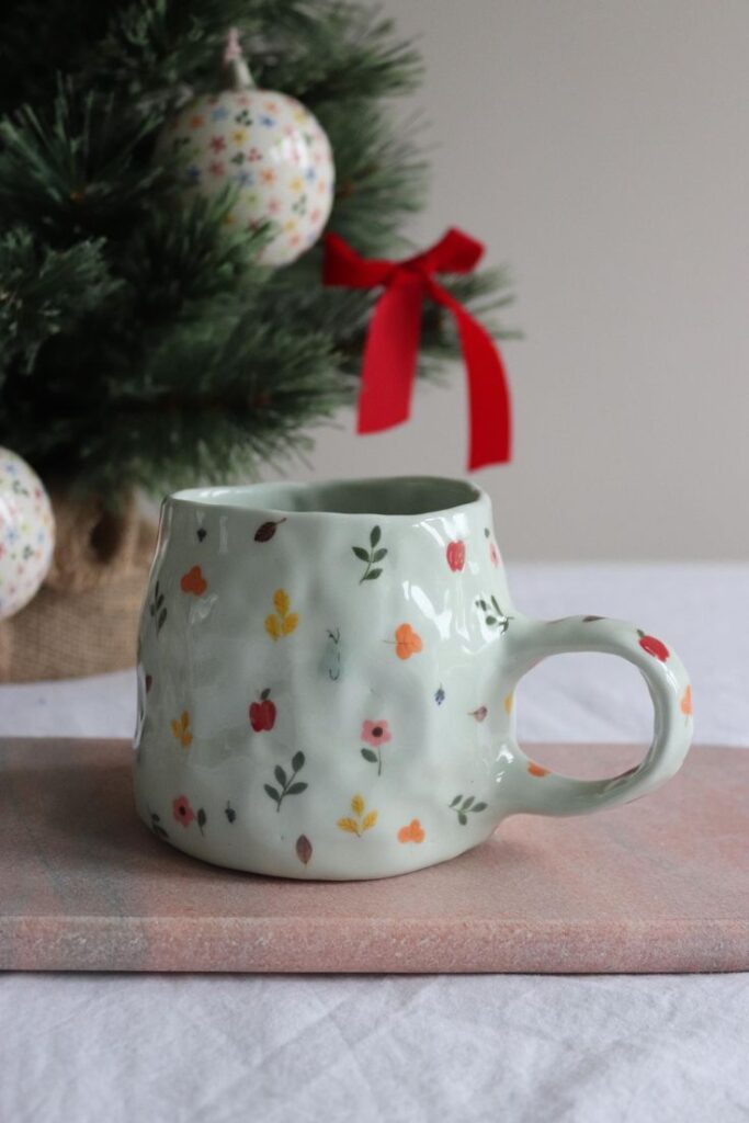 Whimsical floral mug with Christmas tree and ornaments in background, perfect for festive holiday decor.