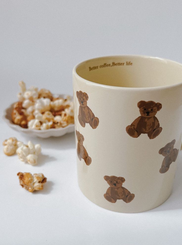 Cute teddy bear mug with Better coffee, Better life text, next to a plate of popcorn. Cozy and adorable.