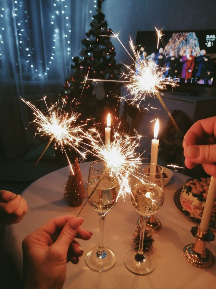 Hands holding sparklers over a festive table setting with candles and champagne, holiday celebration in a cozy room.