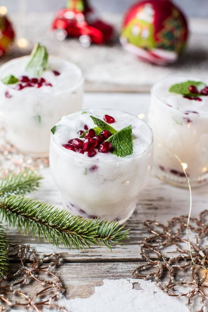 Festive holiday cocktails with pomegranate seeds and mint, surrounded by Christmas ornaments and pine branches.