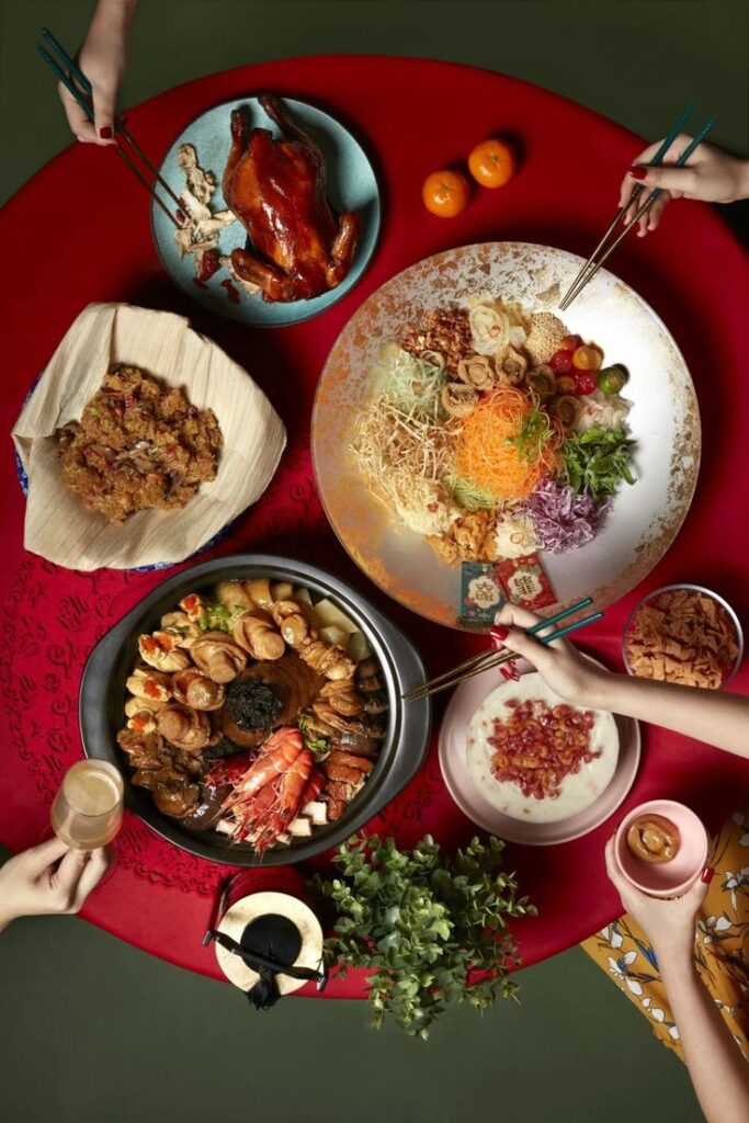 Festive Chinese New Year feast with vibrant dishes and decorations on a red table, including roasted duck and seafood platter.