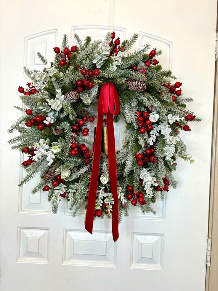 Festive Christmas wreath with red berries, pinecones, and ribbon on a white door.