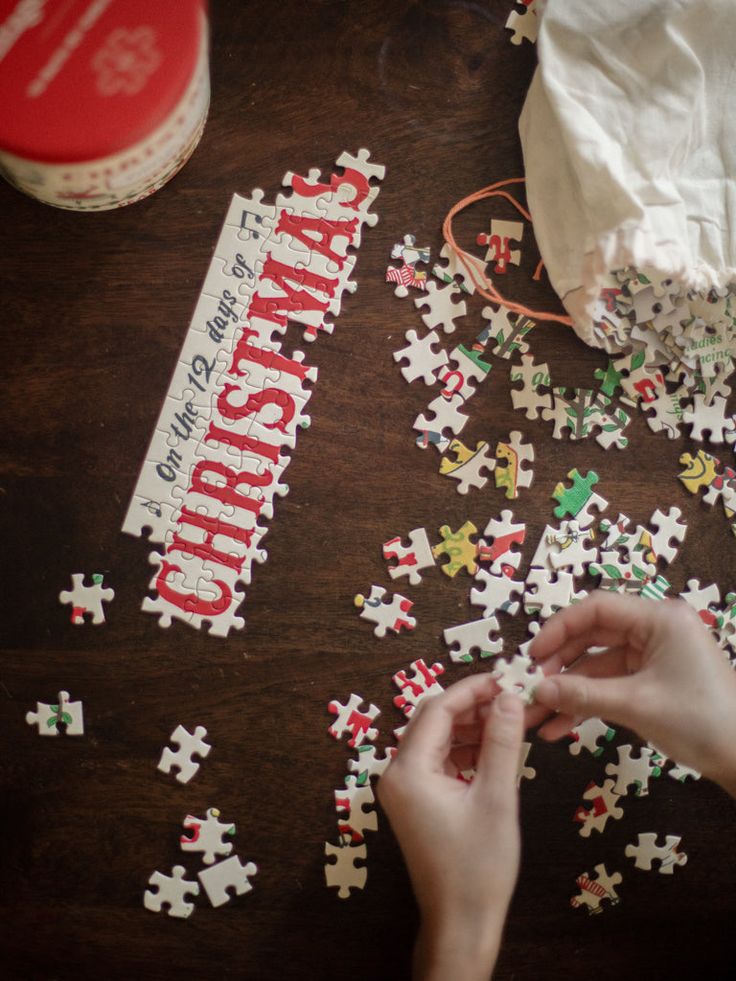 Hands assembling a Christmas-themed puzzle on a dark wooden table.