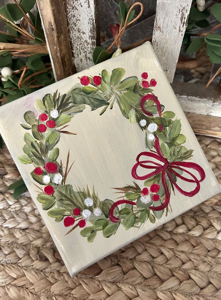 Hand-painted wreath on canvas with red and white berries, accented with a ribbon, perfect for festive decor.