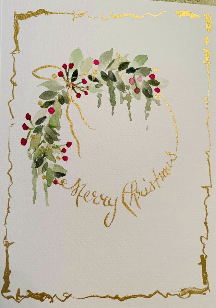 Watercolor Christmas wreath with gold Merry Christmas text on a white card.