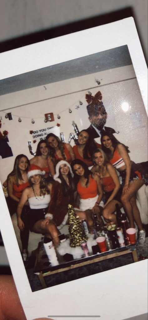 Group of friends in festive holiday outfits smiling at a party with Christmas decorations.