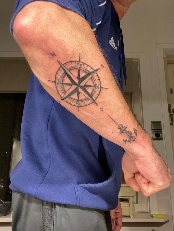 Forearm tattoo featuring a detailed compass and anchor design on a person wearing a blue shirt.