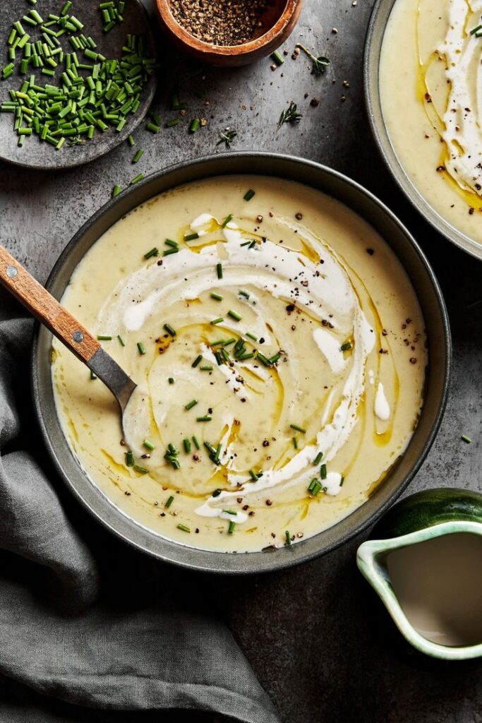 Creamy potato soup garnished with chives, black pepper, and olive oil in a bowl, spoon ready to serve.