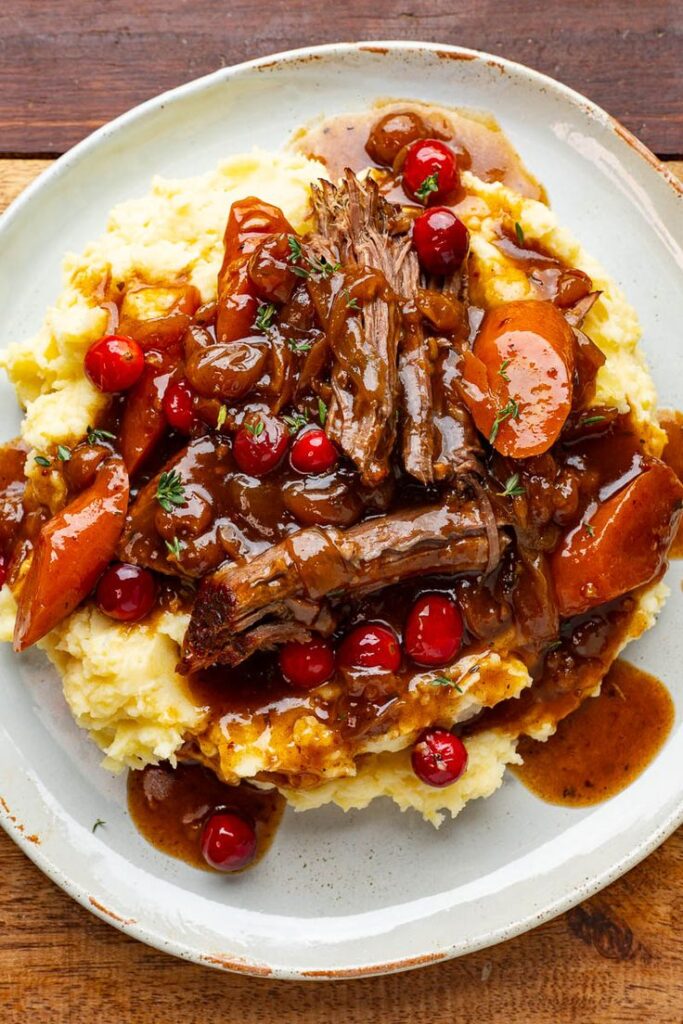 Savory pot roast on creamy mashed potatoes with carrots and cranberries, topped with rich gravy. Perfect comfort food.