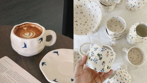 Handcrafted ceramic cups with latte art and floral designs on wooden table and white cloth.