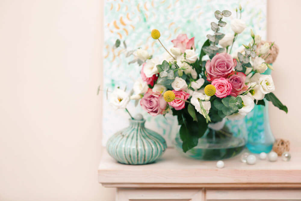 Elegant floral arrangement with pink roses and greenery in a glass vase on a wooden table, next to a decorative vase.